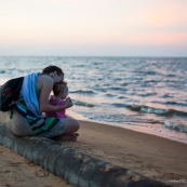 Guyane. Sur la plage des salines (Remire Montjoly) une femme et son bebe en train de regarder le coucher de soleil. Assis sur un tronc de palmier.