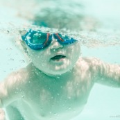 Portrait de bebe sous l'eau. Sa maman a proximite. Bebe avec des lunettes sous l'eau dans une piscine. En train d'apprendre a nager.
