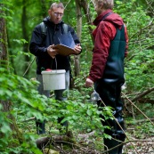 Deux hommes en pleine nature, effectuant un recensement de tritons. Ils ont des bottes et des waders, un seau et un carnet dans lequel ils notent leurs observations. Il sont au bord d'une mare. Etude de la variation de population d'amphibiens. Protection des espËces, suivi des populations, dans le cadre d'un contrat Natura 2000.