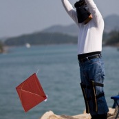 Pilote de cerf-volant traditionnel ‡ Hong-Kong, en Chine. Entrainement au cerf-volant de combat monofil mais directif. VisiËre pour se protÈger du Soleil, et Èquipement complet pour piloter le cerf-volant, au bord de la mer. Pilote debout, en train de prÈparer son cerf-volat, rouge. DÈvidoir en main il s'apprete ‡ le mettre en vol. Il est ÈquipÈ pour piloter son cerf-volant.