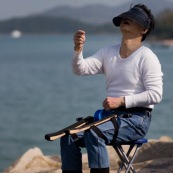 Pilote de cerf-volant traditionnel ‡ Hong-Kong, en Chine. Entrainement au cerf-volant de combat monofil mais directif. VisiËre pour se protÈger du Soleil, et Èquipement complet pour piloter le cerf-volant, au bord de la mer. Pilote assis sur une chaise, avec le dÈvidoir en main, roulant sur des supports attachÈs aux cuisses, et permettant de rembobiner ou dÈbobiner avec rapiditÈ le fil.