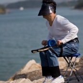 Pilote de cerf-volant traditionnel ‡ Hong-Kong, en Chine. Entrainement au cerf-volant de combat monofil mais directif. VisiËre pour se protÈger du Soleil, et Èquipement complet pour piloter le cerf-volant, au bord de la mer. Pilote assis sur une chaise, avec le dÈvidoir en main, roulant sur des supports attachÈs aux cuisses, et permettant de rembobiner ou dÈbobiner avec rapiditÈ le fil.