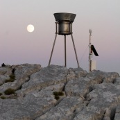 Station meteorologique en montagne avec la lune en arriere plan, paysage lunaire. Pluviometre.