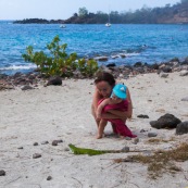 Guadeloupe. Tourisme. Sur la plage au bord de la mer. Femme et son bebe en train d'observer un iguane. Iguana iguana. Iguane vert. Iguane commun. Enfant.