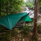 Carbet bache en foret tropicale amazonienne en Guyane. Hamac tendu entre deux arbres et bache tendue au dessus pour passer la nuit. Camping. Chute d'eau en arriere plan.
