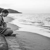 Guyane. Sur la plage des salines (Remire Montjoly) une femme et son bebe en train de regarder le coucher de soleil. Assis sur un tronc de palmier.