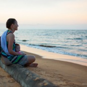 Guyane. Sur la plage des salines (Remire Montjoly) une femme et son bebe en train de regarder le coucher de soleil. Assis sur un tronc de palmier.