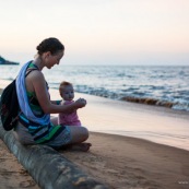 Guyane. Sur la plage des salines (Remire Montjoly) une femme et son bebe en train de regarder le coucher de soleil. Assis sur un tronc de palmier.