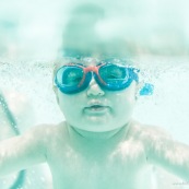 Portrait de bebe sous l'eau. Sa maman a proximite. Bebe avec des lunettes sous l'eau dans une piscine. En train d'apprendre a nager.