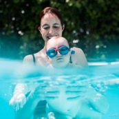 Bebe dans une piscine avec sa maman. En train d'apprendre a nager. Avec des lunettes de piscine.
