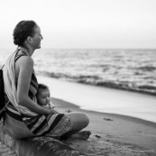 Guyane. Sur la plage des salines (Remire Montjoly) une femme et son bebe en train de regarder le coucher de soleil. Assis sur un tronc de palmier.