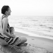 Guyane. Sur la plage des salines (Remire Montjoly) une femme et son bebe en train de regarder le coucher de soleil. Assis sur un tronc de palmier.