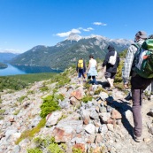 Randonnée en Patagonie : guide et touristes. Sac au dos, en montagne. Vue de derrière. En descente vers un immense lac.