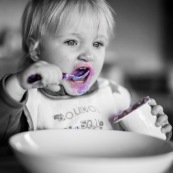 Bebe petite fille enfant en train de manger un yaourt a la myrtille.